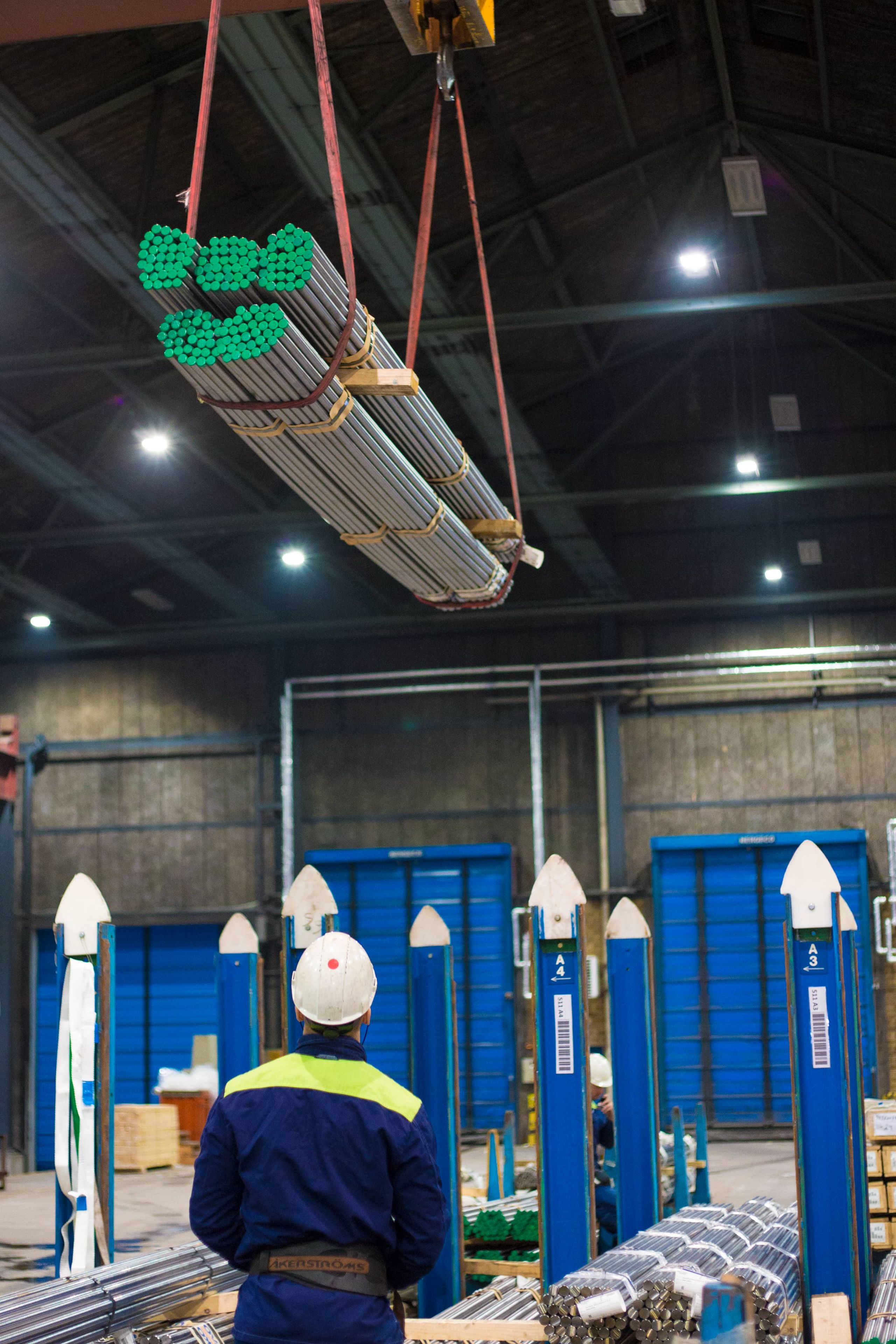 An Ovako operator watches an overhead crane lift a bundle of steel bar at the Hällefors mill.